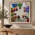 A framed art print featuring a circular collage of diverse men in colorful African patterned clothing, displayed on a light beige wall above a wooden console table with decorative items.