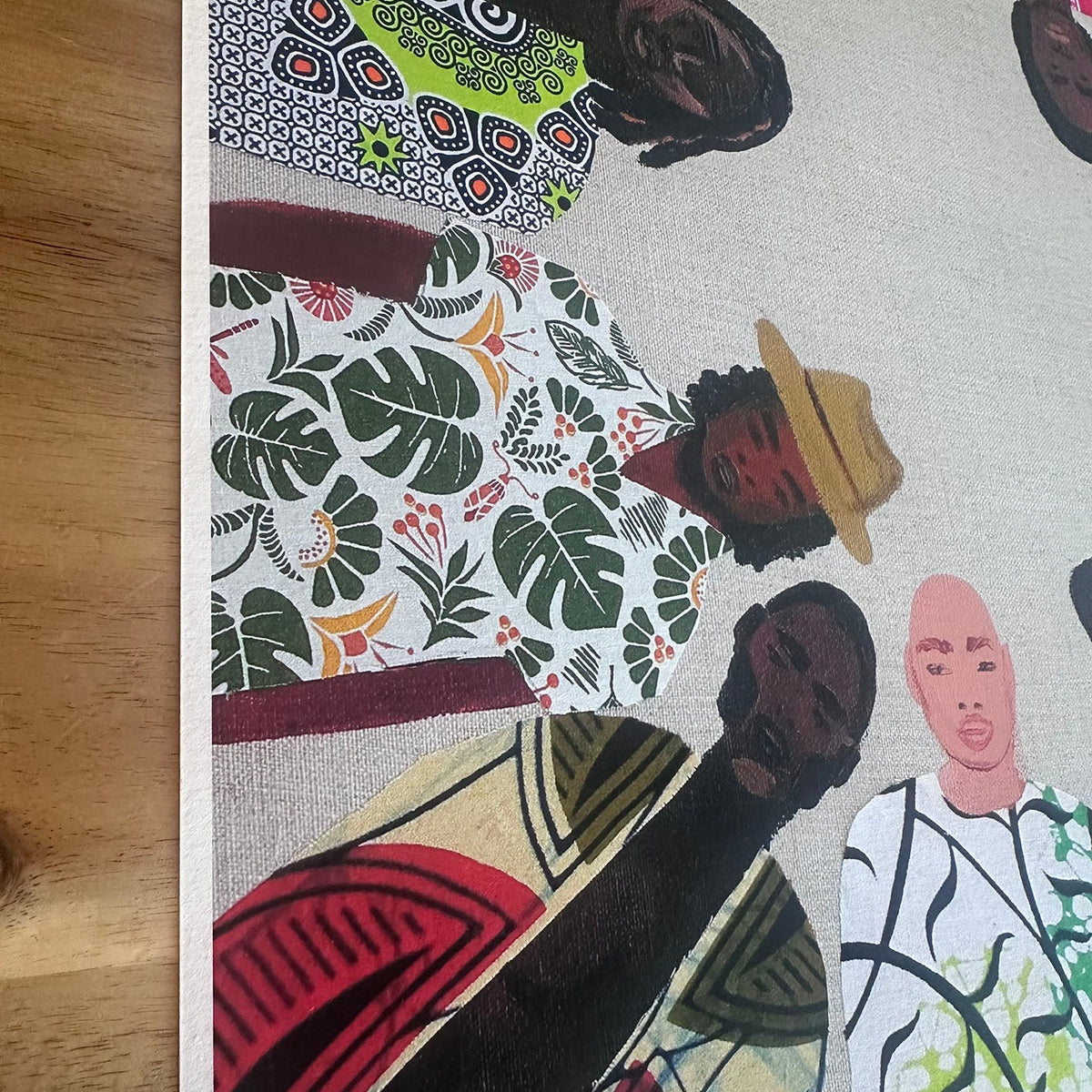 A close-up of a printed artwork showing stylized illustrated figures in colourful clothing and patterned African inspired garments, photographed on a light wood floor.
