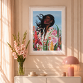 A framed art print featuring a colorful portrait of a woman surrounded by flowers, displayed on a beige wall above a modern sofa in a styled living room.